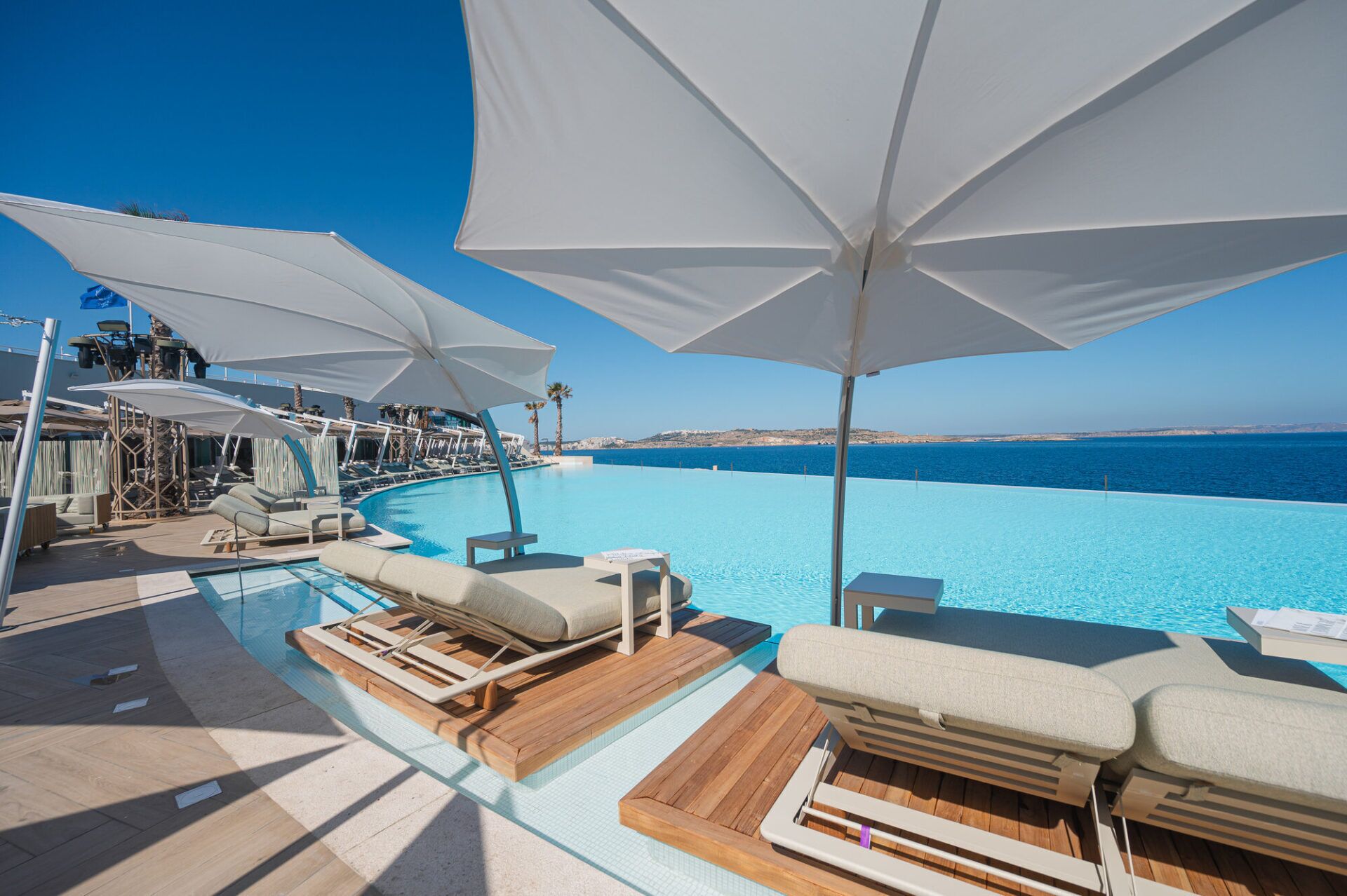 A poolside area with lounge chairs and umbrellas, overlooking a clear blue sea.