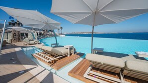 A poolside area with lounge chairs and umbrellas, overlooking a clear blue sea. - Coastal Vibes: 3BR Holiday Apartment, Bugibba (Saint Paul's Bay)