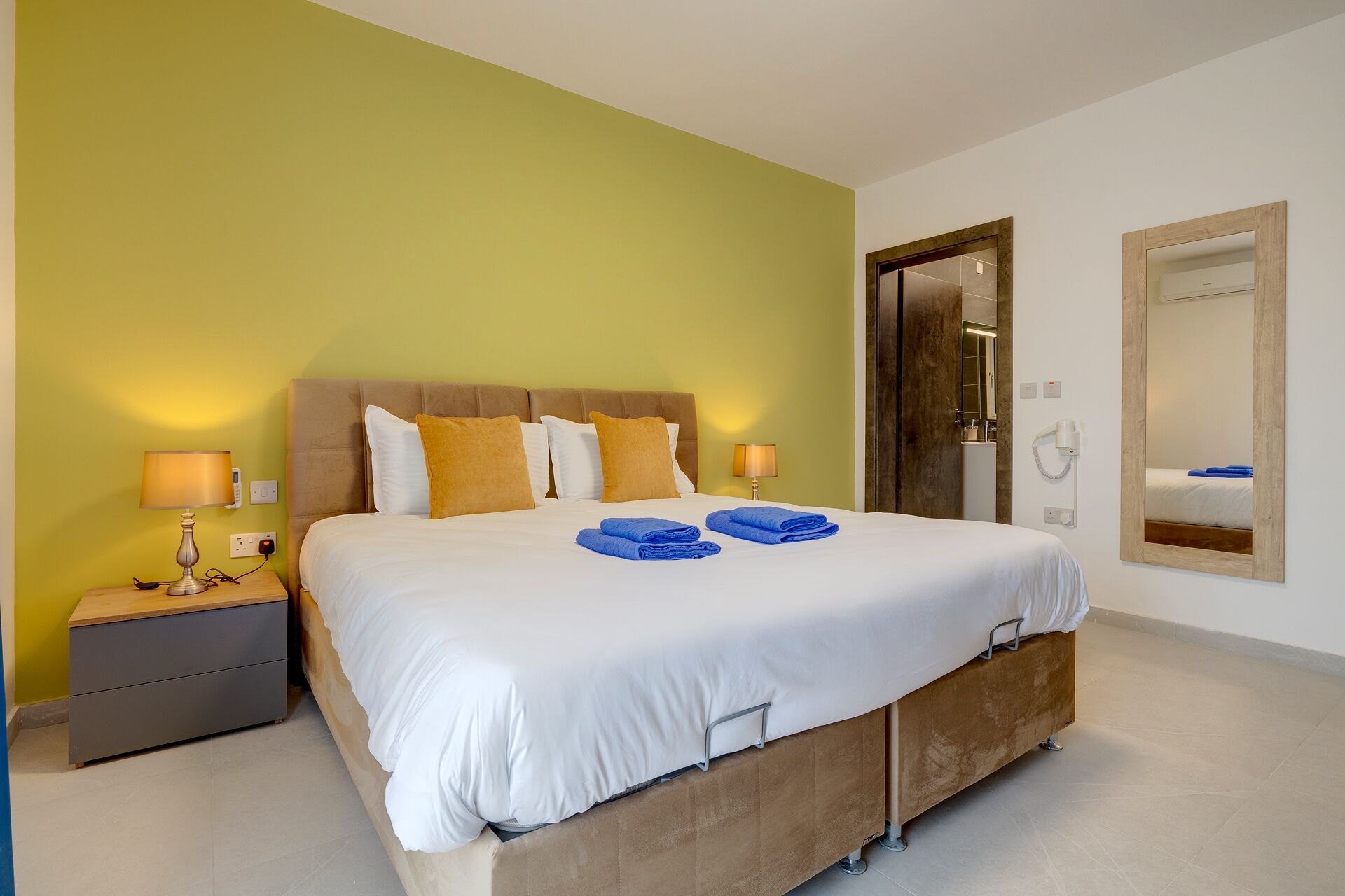 A hotel room with a bed, bedside tables, a mirror, and a door.
