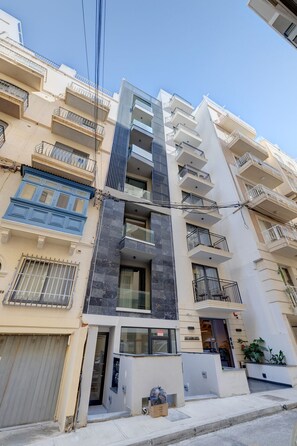 Un immeuble résidentiel à plusieurs étages, doté de balcons, d’une entrée au niveau du sol et d’une devanture visible.
