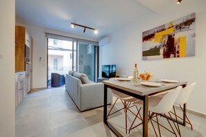 Un espace de repas moderne avec une table dressée pour deux personnes, un canapé et un téléviseur en arrière-plan.