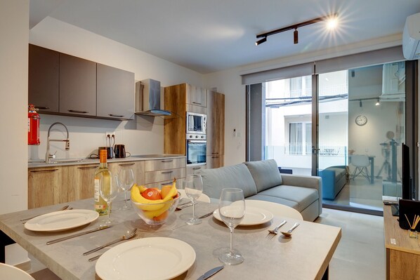 Une cuisine moderne avec un coin repas aménagé pour le dîner, comprenant une table mise avec des assiettes, des verres et un panier de fruits.