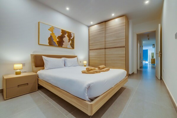 A modern hotel room with a large bed, wooden headboard, and a view of the hallway.