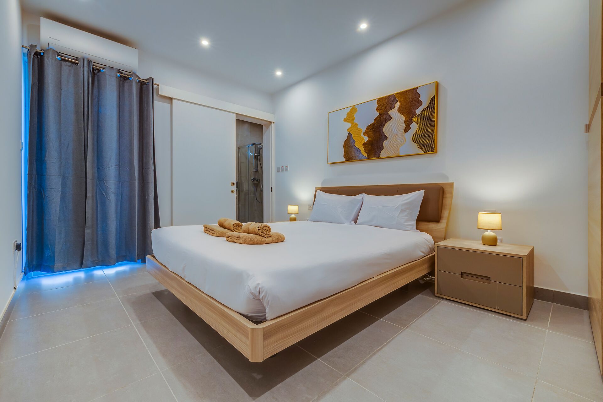 Une chambre d’hôtel avec un grand lit, une table de chevet avec une lampe, un espace douche et un tableau au mur.