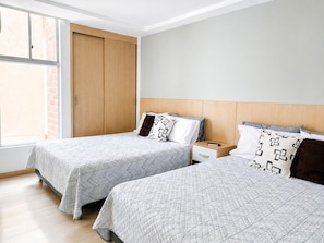 A hotel room with two beds, a wooden wardrobe, a nightstand, and a window with a view of a brick building. - Medellin, Bring your toothbrush, in Laureles (Medellín)