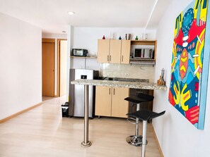 A compact kitchen with a microwave, toaster, and a small refrigerator. There are two bar stools and a painting on the wall. - Medellin, Bring your toothbrush, in Laureles (Medellín)