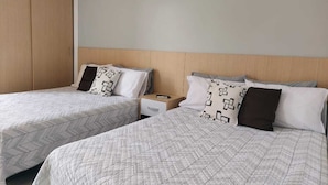 Dos camas individuales con ropa de cama estampada, un armario de madera y una mesita de noche con un control remoto.