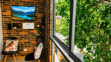Una habitación con pared de ladrillo, un ventanal grande, un escritorio, una silla y un cuadro.