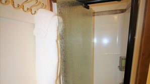 Une salle de bain avec une porte de douche en verre, une serviette suspendue à un crochet et un cadre en bois autour de la porte.