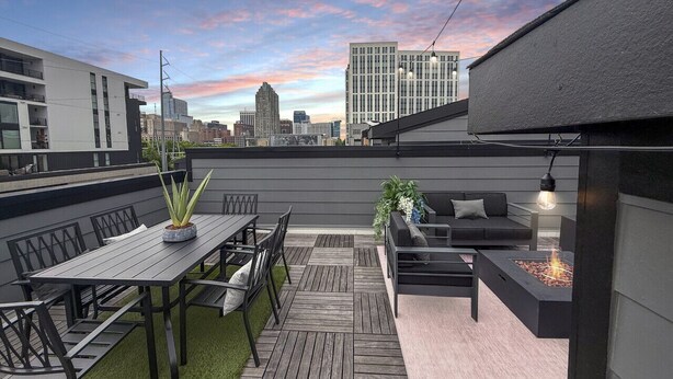 A rooftop patio with a dining table, chairs, a sofa, and a fire pit.