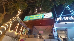 A building with a neon sign for 'Laxmi Dormitory' and another sign for 'AXMIPAL'. - Laxmi Dormitory | 2 mins walk from Prem Mandir (Vrindavan)