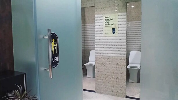 A public restroom with a 'Toilets' sign, a 'Flush the toilet after each use' sign, and a 'Push' sign on the door. - Laxmi Dormitory | 2 mins walk from Prem Mandir (Vrindavan)