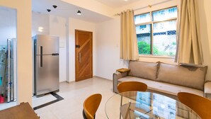 A modern living room with a glass dining table, a sofa, and a built-in refrigerator. - SUH Copacabana 97 Metro Near Ipanema (Rio de Janeiro)