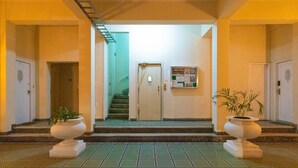 A hallway with a tiled floor, two potted plants, a door with a sign, and a staircase leading to an upper level. - SUH Copacabana 97 Metro Near Ipanema (Rio de Janeiro)