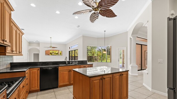 A spacious kitchen with wooden cabinets, a black countertop, and a ceiling fan. - Sun, Sand & Space: Your Bradenton Vacation Home with Private Pool (Bradenton)