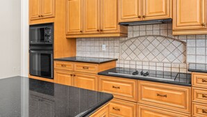 A kitchen with wooden cabinets, a black countertop, and a tiled backsplash. - Sun, Sand & Space: Your Bradenton Vacation Home with Private Pool (Bradenton)