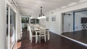A spacious dining area with a long table and chairs, a kitchen in the background, and a large window providing natural light. - Rowdy Rooster ~Steps to Atlantic ~ Hot Tub (Delray Beach)
