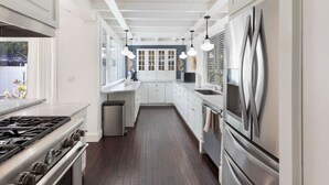 A narrow kitchen with white cabinets, a stainless steel refrigerator, and a gas stove. - Rowdy Rooster ~Steps to Atlantic ~ Hot Tub (Delray Beach)