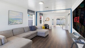 A spacious living area with a large sectional sofa, a dining table with chairs, and a wall-mounted TV. - Rowdy Rooster ~Steps to Atlantic ~ Hot Tub (Delray Beach)