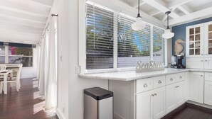 A modern kitchen with white cabinetry, a built-in island, and a window with blinds. - Rowdy Rooster ~Steps to Atlantic ~ Hot Tub (Delray Beach)