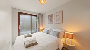 A modern bedroom with a large bed, bedside lamps, and a view through a sliding glass door. - NÔA curacao (Willemstad)