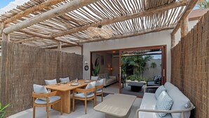 An outdoor patio with a wooden dining table and chairs, a sofa, and a pergola overhead. - NÔA curacao (Willemstad)