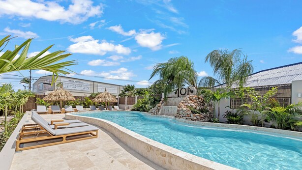 A swimming pool with lounge chairs, a stone wall, and tropical plants. - NÔA curacao (Willemstad)