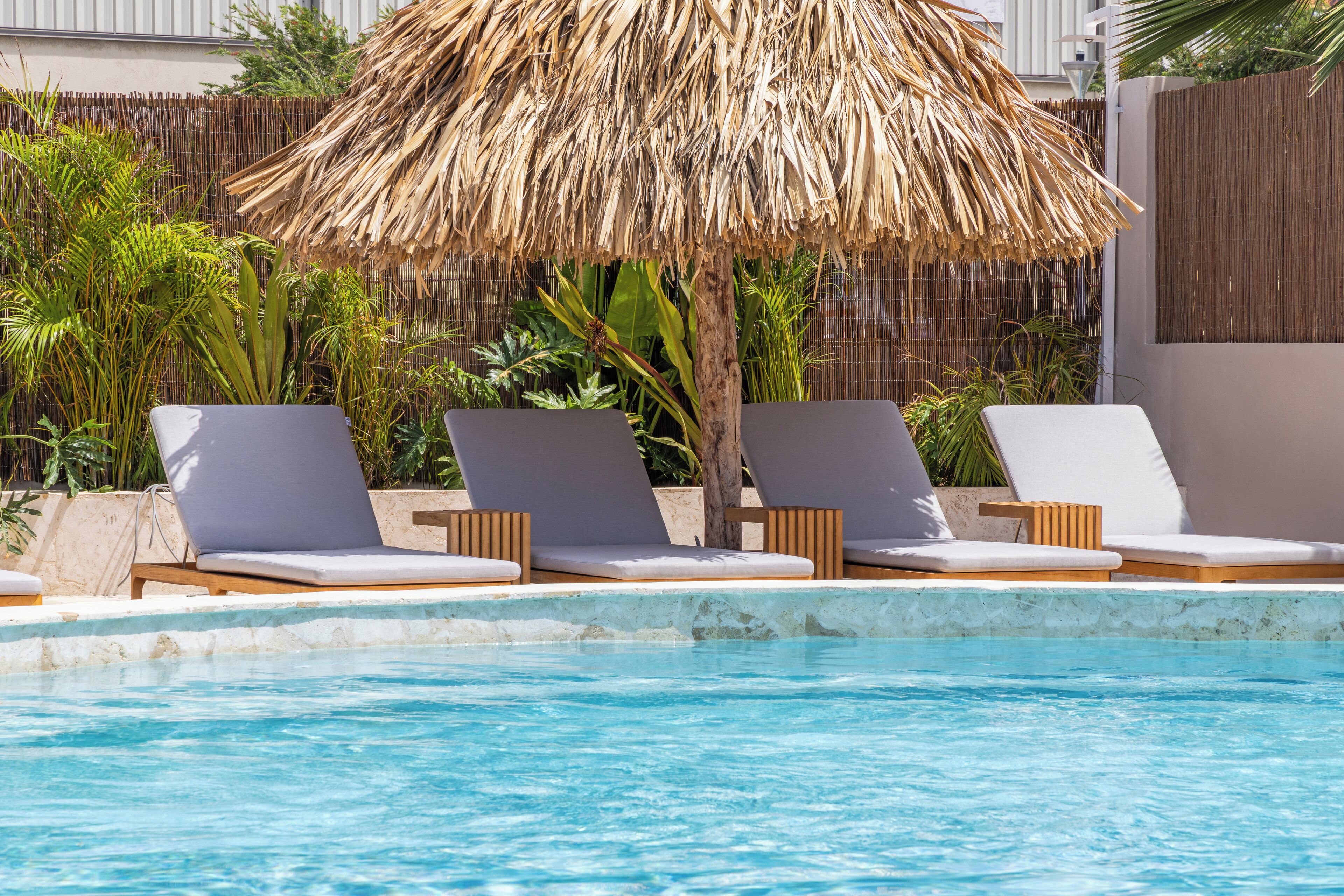 A pool area with lounge chairs and a thatched umbrella.