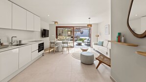 A modern kitchen with white cabinets, a built-in oven, and a large island with seating. There is a dining area with a table and chairs, and a large mirror on the wall. - NÔA curacao (Willemstad)