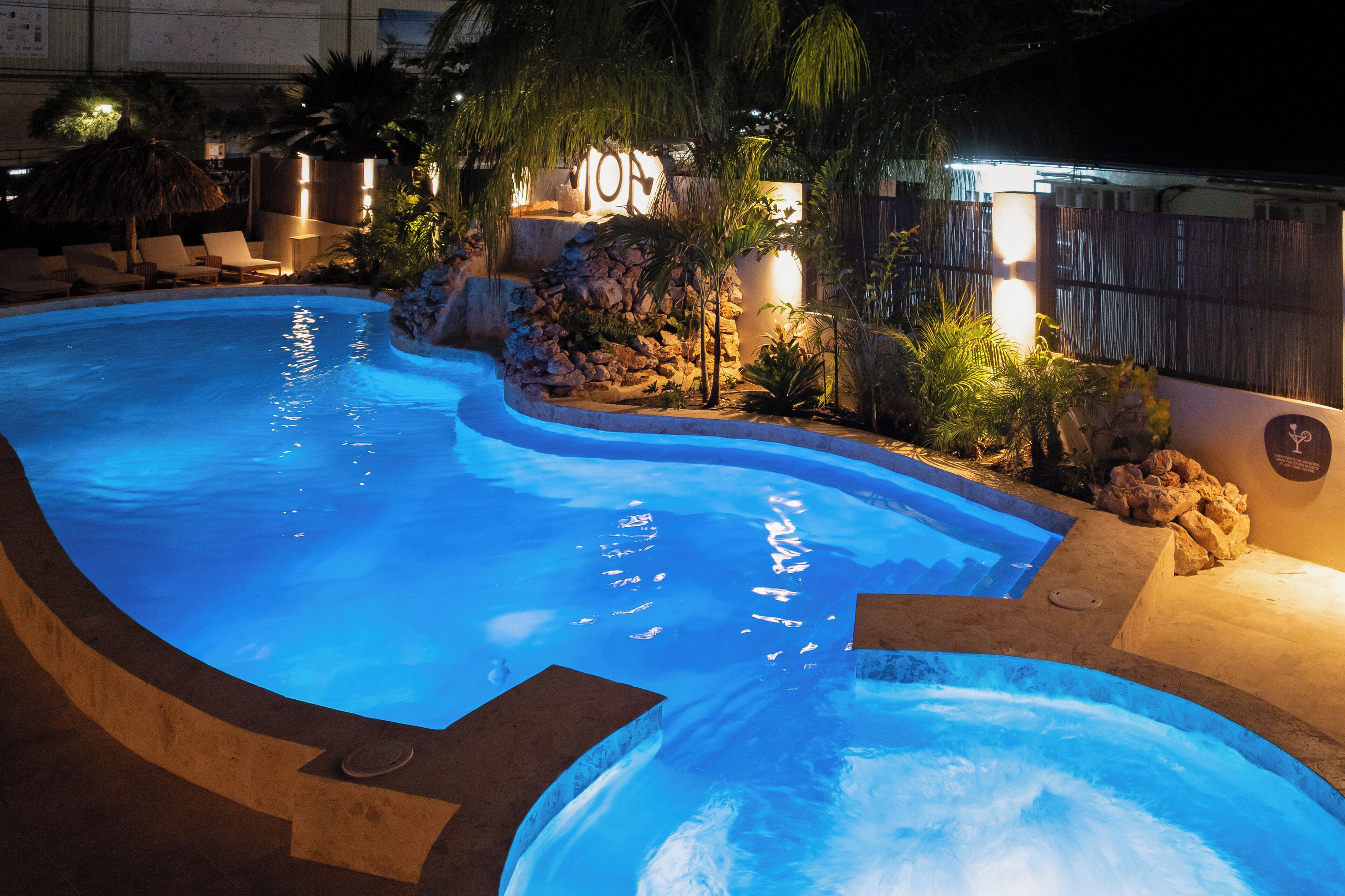 Una piscina de disseny corbat, envoltada de roques i plantes, il·luminada per una llum càlida.