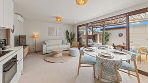 A modern kitchen with white cabinets, a dining area with a round table and patterned chairs, and a large window with a view of the outdoors. - NÔA curacao (Willemstad)