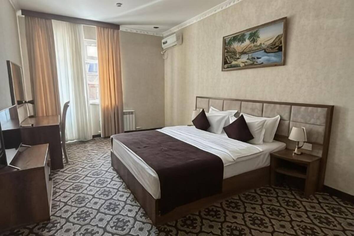 A hotel room with a bed, a desk, a lamp, and a painting on the wall.