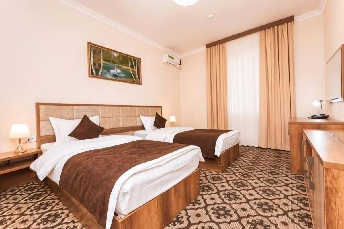 A hotel room with two beds, a wooden headboard, a desk with a mirror, and a patterned carpet.