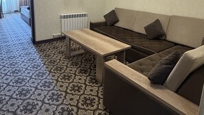 Una habitación con alfombra estampada, un sofá con cojines, una mesa de madera y un radiador.