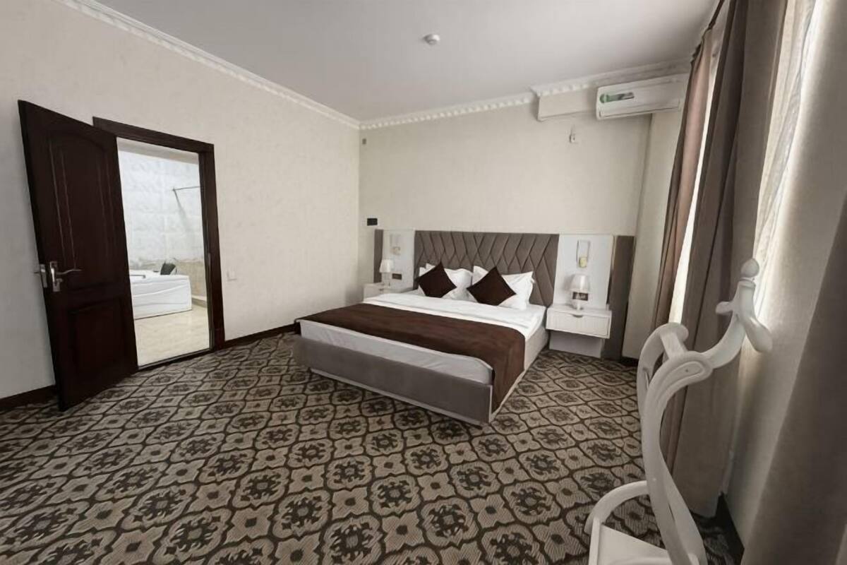 A hotel room with a bed, a chair, a desk, and a door leading to a balcony.