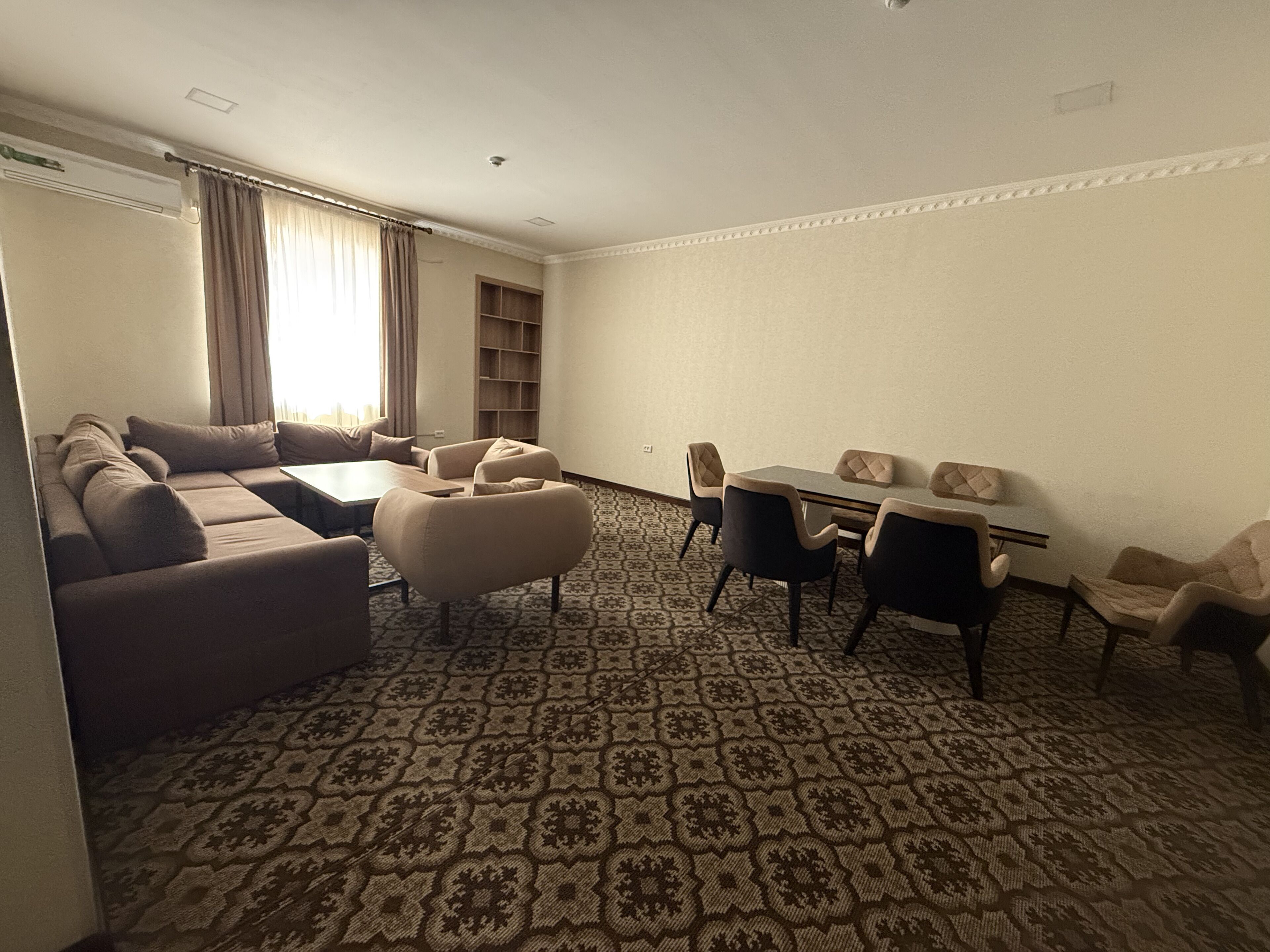 A living room with a sofa, ottoman, dining table, chairs, and a patterned carpet.