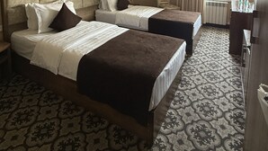 Una habitación de hotel con dos camas, una araña, un cuadro en la pared y un ventanal con cortinas.