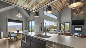 Une cuisine moderne dotée d’un grand îlot central, d’appareils électroménagers en acier inoxydable et offrant une vue sur les montagnes.