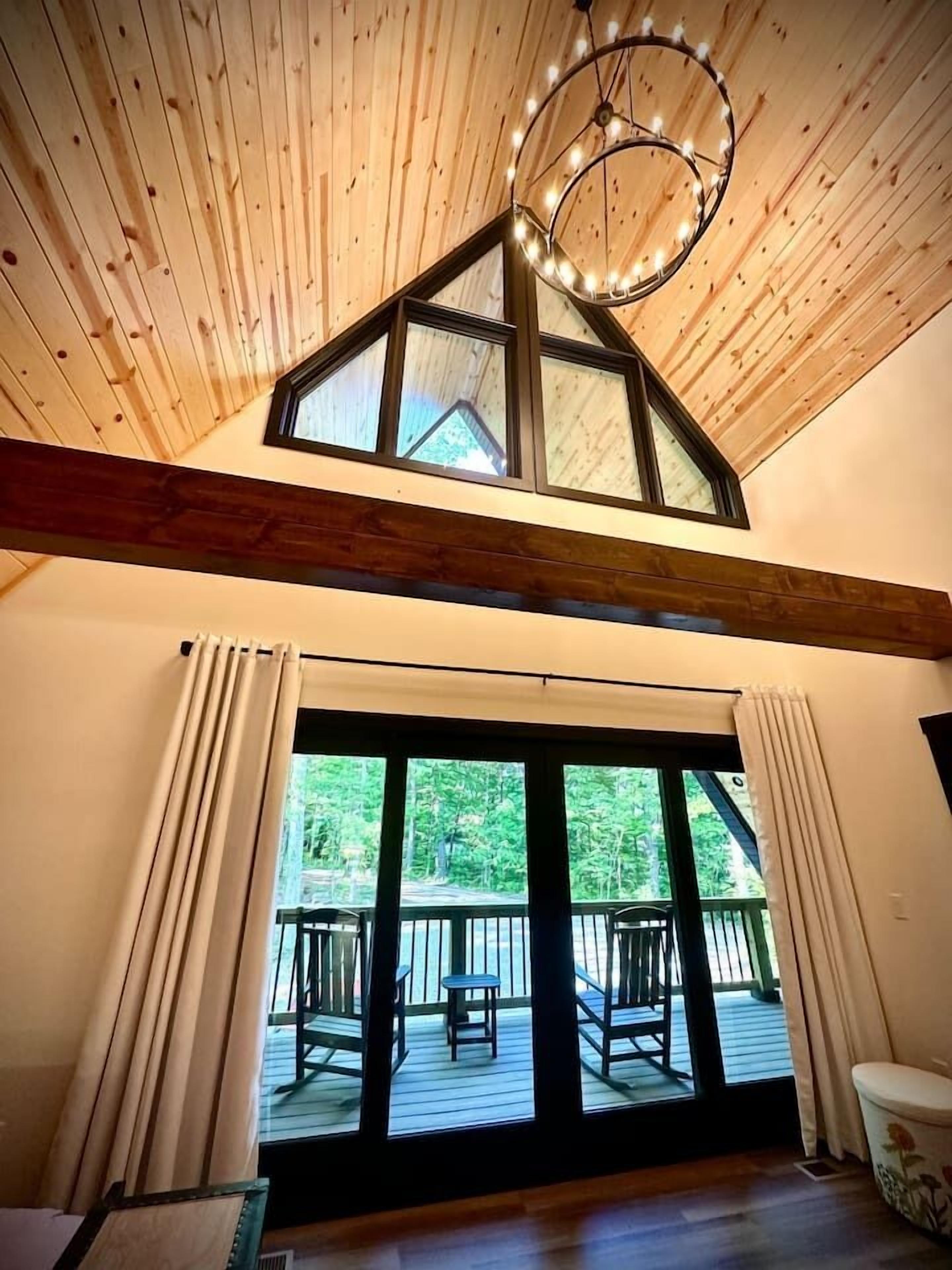 Una habitación con techo inclinado, ventanas amplias, techo de madera y vistas a una terraza exterior.