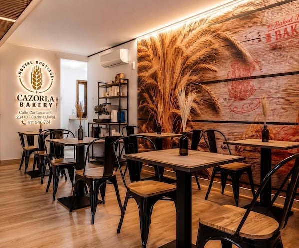 A cozy bakery interior with wooden tables and chairs, a large wheat-themed mural, and a visible counter with baked goods.