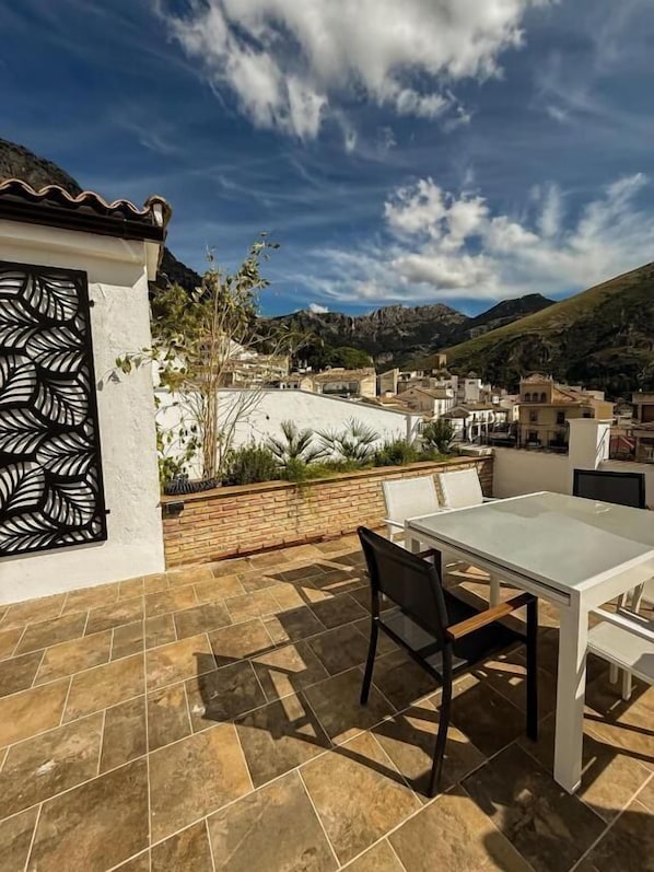 Une terrasse avec une table et des chaises, une porte décorative et une vue sur la ville et les montagnes.