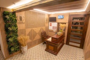 A reception area with a wooden desk, a chair, a wall-mounted TV, and a door.