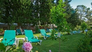 A garden with green lounge chairs, a small tree, and a pink rose.