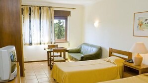A hotel room with two beds, a television, a desk, a chair, and a window with curtains.