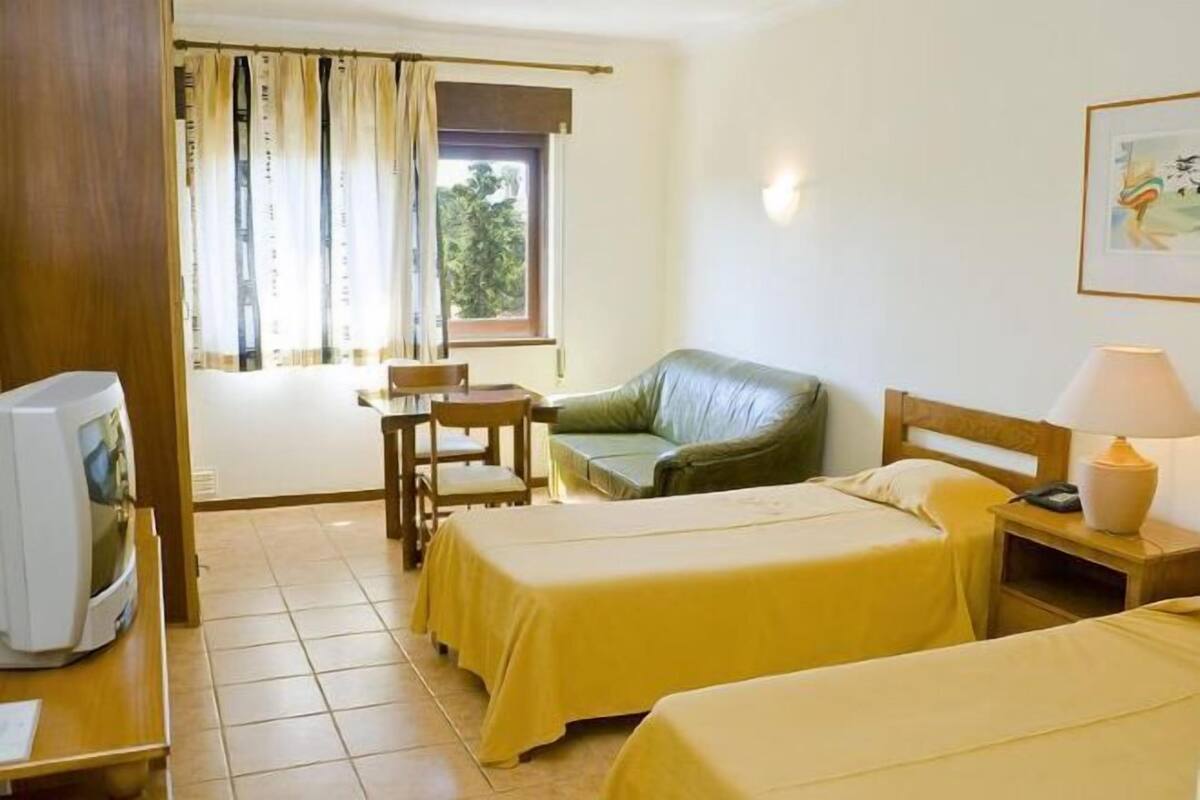 Une chambre d’hôtel avec deux lits, une télévision, un bureau, une chaise et une fenêtre avec des rideaux.