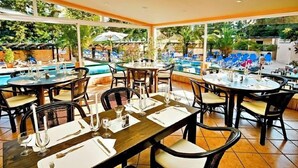 An outdoor dining area with tables set for guests, a pool in the background, and a view of the surrounding greenery. - Hotel Balaia Mar (Olhos de Agua)