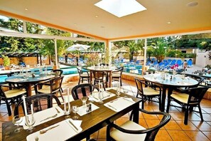 An outdoor dining area with tables set for guests, a pool in the background, and a view of the surrounding greenery. - Hotel Balaia Mar (Olhos de Agua)