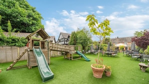 A backyard with a wooden play structure, a green slide, and a seating area with tables and chairs.