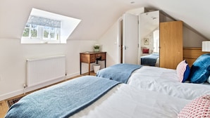 A bedroom with a sloped ceiling, a window, a radiator, a desk, and a wardrobe.