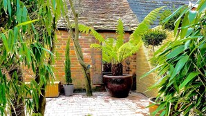 A courtyard with a brick floor, potted plants, and a brick wall with a tiled roof. - Peppercorn  An Enchanting house in Lymington (Hampshire)